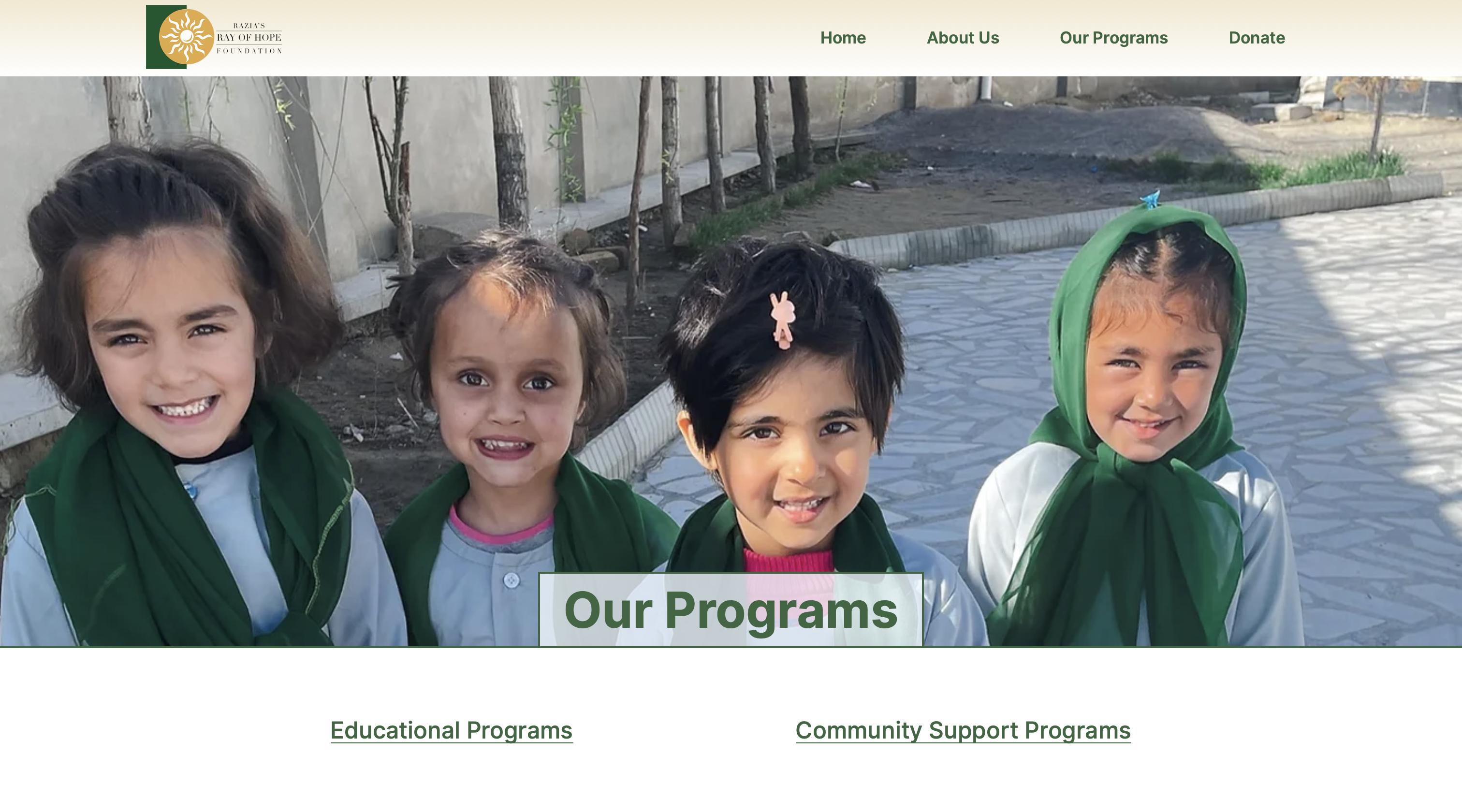 Four young girls wearing uniforms, smiling and standing together outdoors on a sunny day. The image is part of the 'Our Programs' section of the Razia's Ray of Hope Foundation project website.